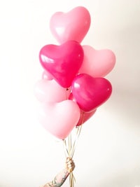 a person holding pink and pink heart shaped balloons