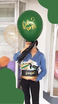 a woman holding a green balloon in front of a gift box