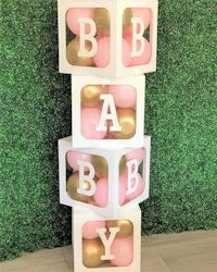 a pink and gold baby shower block with balloons on top