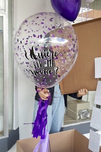 a woman is holding a purple confetti balloon