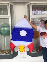 a woman holding up a rocket pinata in front of a store