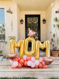 a gold and pink balloon sign with the word mom in front of a house