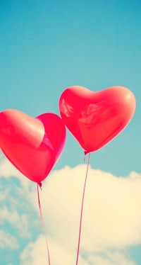 two red heart shaped balloons in the sky