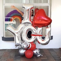 a woman standing next to a heart shaped balloon with i love you written on it